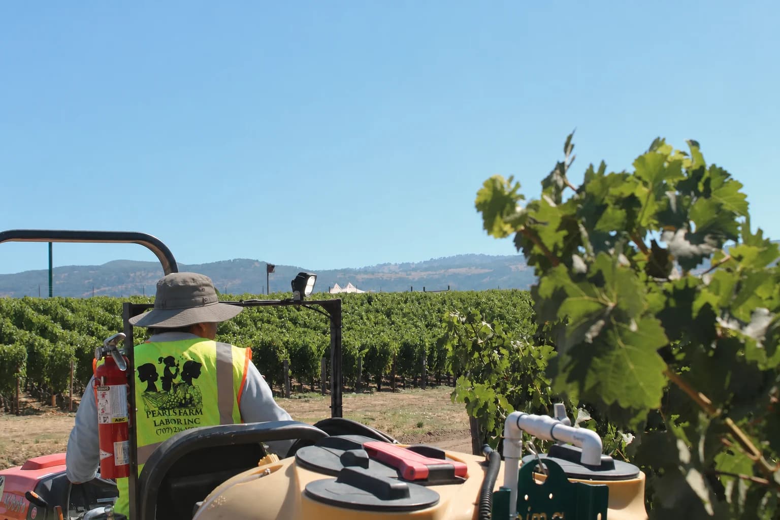 Pearls field operator in a wide-brim hat and long sleeves driving vineyard equipment